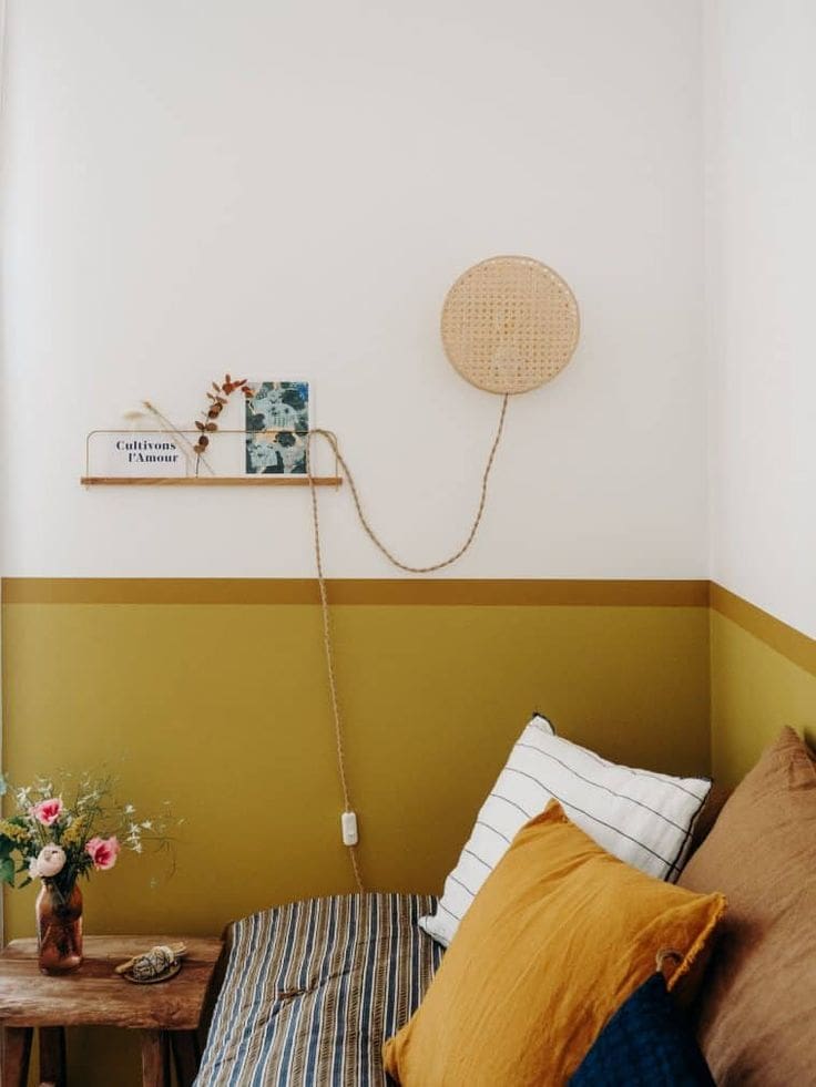 Half painted wall in white at the top and ochre yellow to the bottom. Day bed against wall with various striped and plain throw pillows and cushions