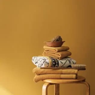 Golden-yellow accent wall with wooden stool in front with folder yellow bath towels and a pot plant