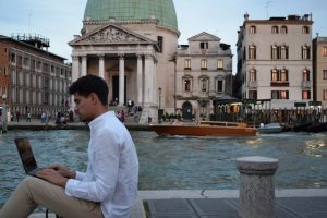 man working on a laptop in front of Venice's canals, taking advantage of the new italy digital nomad visa