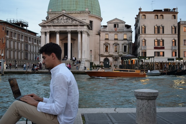 man working on a laptop in front of Venice's canals, taking advantage of the new italy digital nomad visa