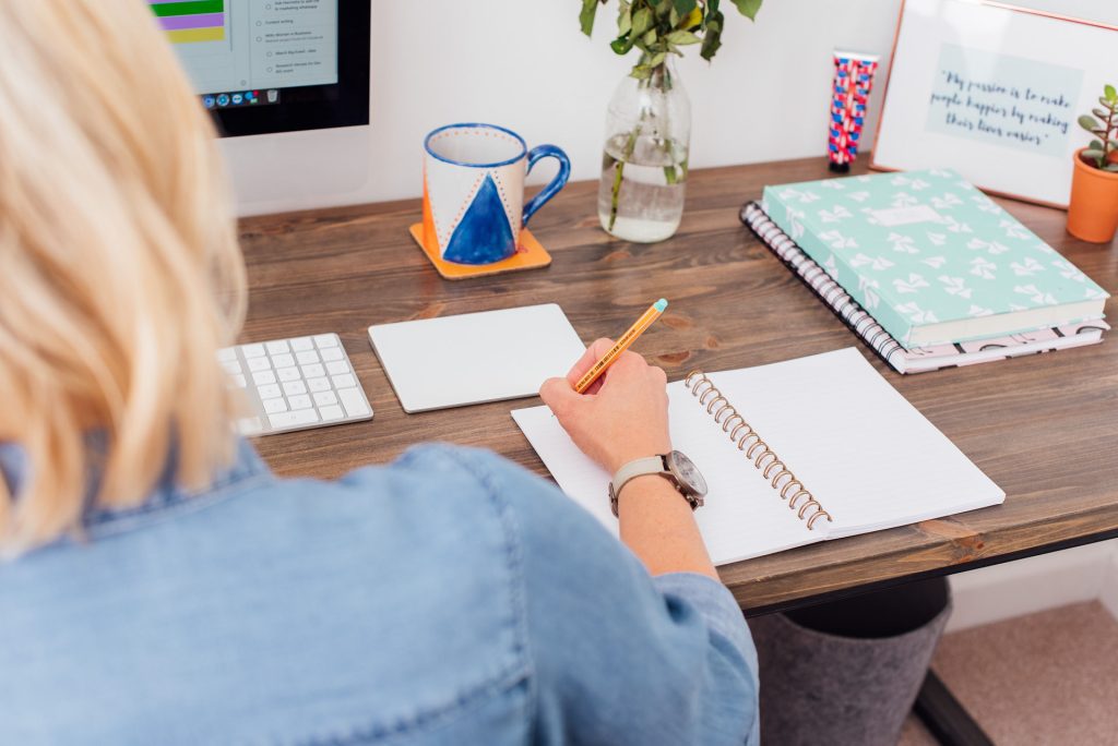 Woman sitting at desk writing in a note pad.
